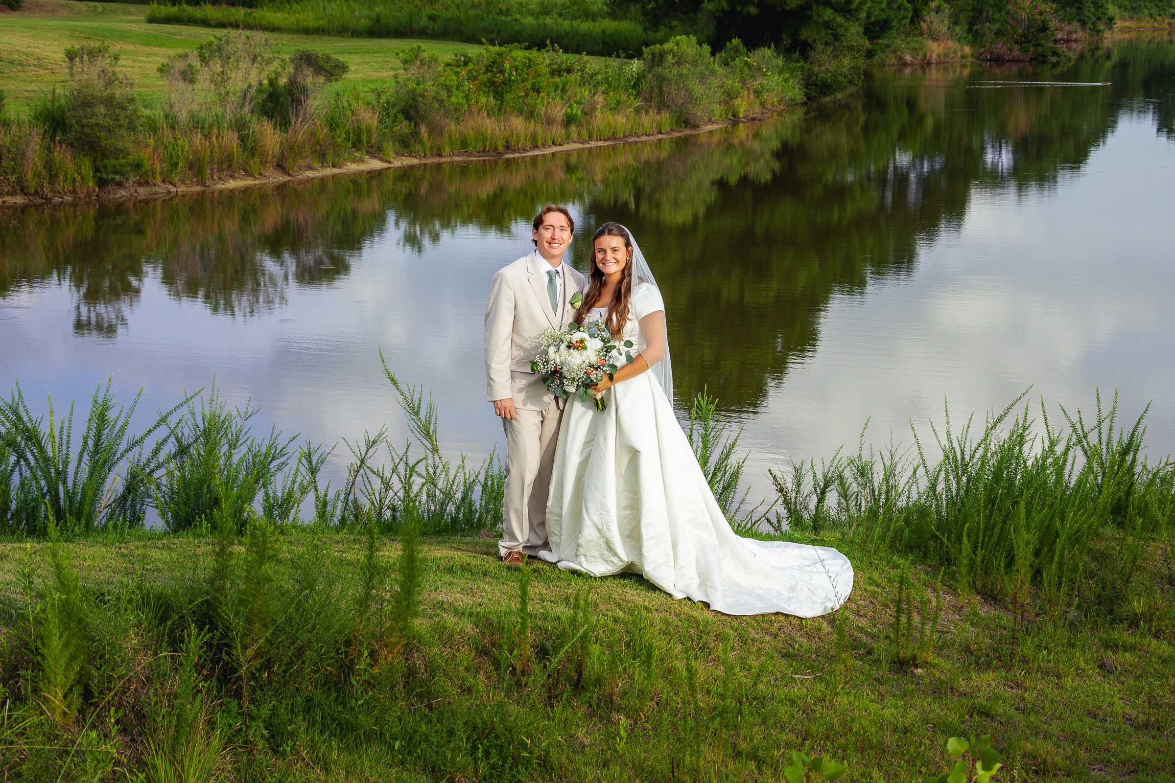 Jenna and Joshua posing for a wedding portrait by the lake at The Venue at Cahoon